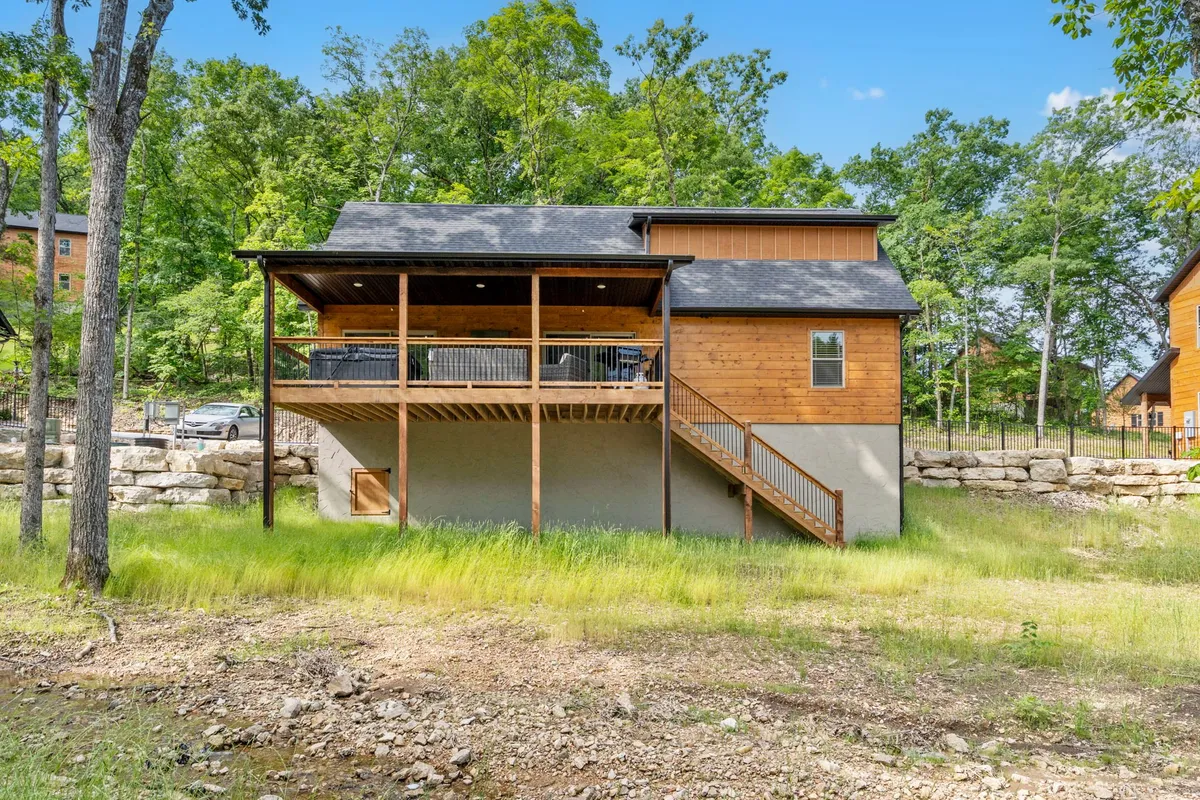 This image features a spacious wooden deck attached to a rustic exterior, surrounded by mature trees that provide privacy and immersion in nature. The deck appears large enough for gatherings and relaxation, with the forested backdrop enhancing the sense of seclusion.