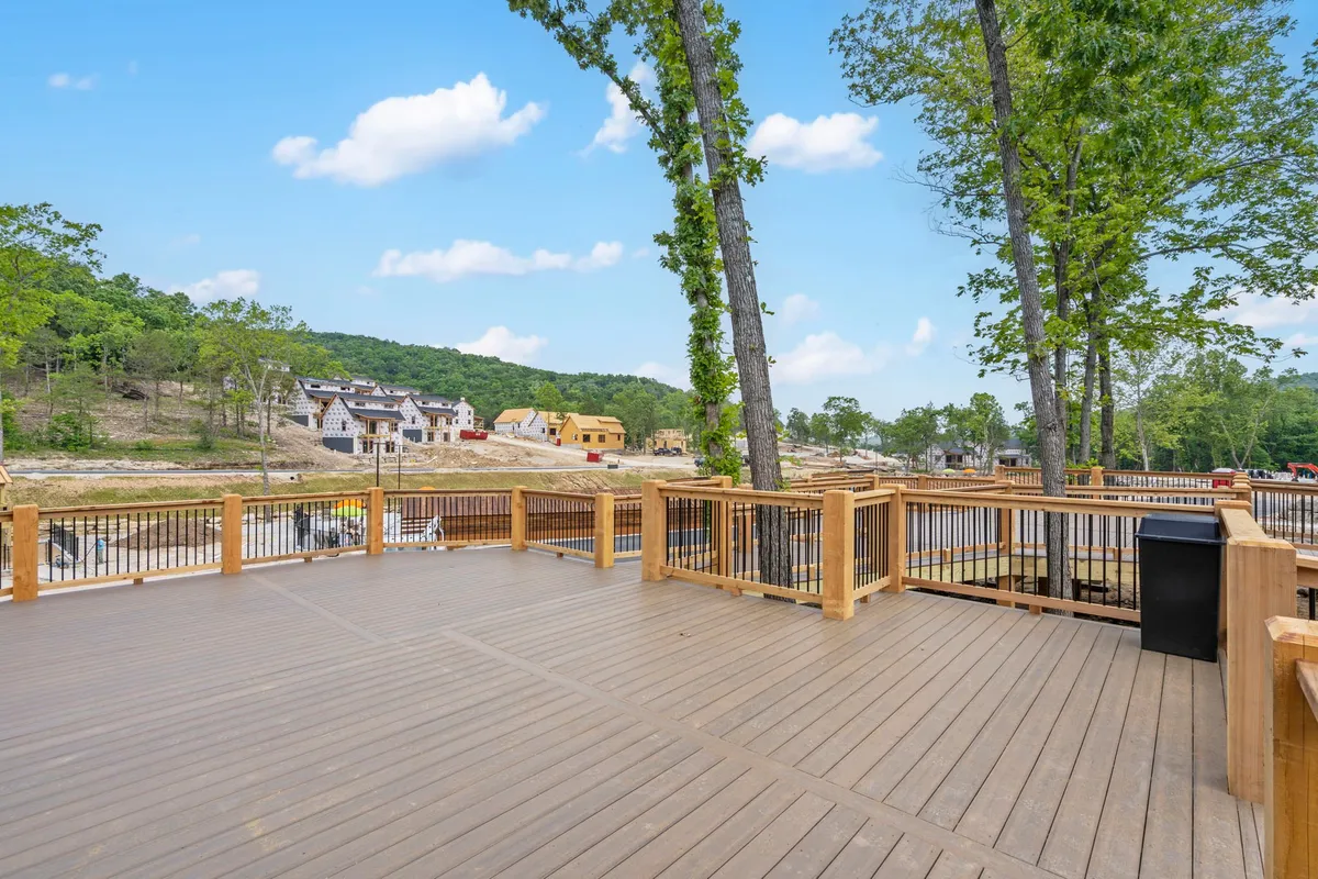 A deck stretches out amidst the trees, featuring seating arrangements ideal for entertaining or simply enjoying nature. The setting is tranquil, with views of neighboring homes in the distance but maintaining a feeling of privacy and serenity.