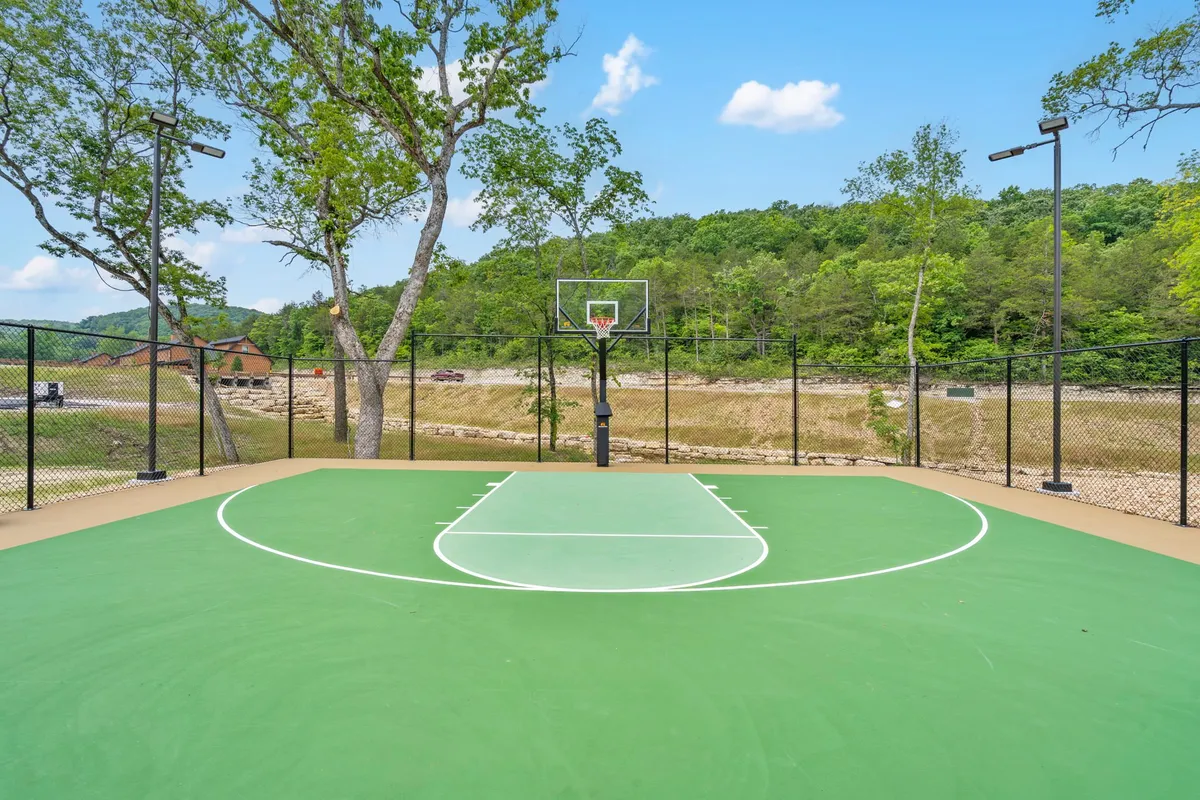 A fenced basketball court surrounded by trees, featuring a basketball hoop and green playing surface. The setting is energetic and playful, inviting guests to enjoy friendly basketball matches, community tournaments, or family activities outdoors.