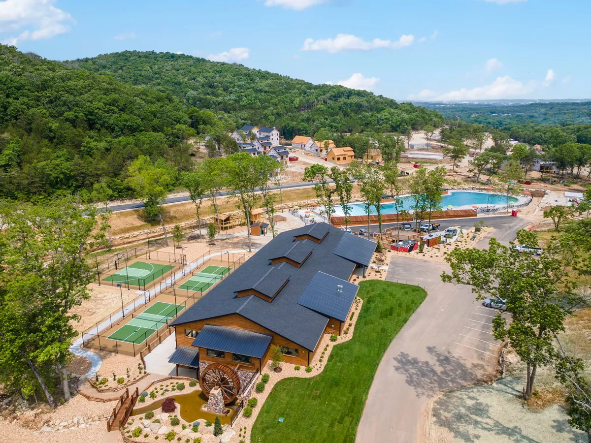 This exterior image captures the main building surrounded by lush gardens, with clear views of both a swimming pool and tennis courts. Families can be seen enjoying the pool and courts, suggesting a lively, communal resort atmosphere. The landscaped gardens and bright setting reinforce the energetic and inviting vibe of the resort's amenities.