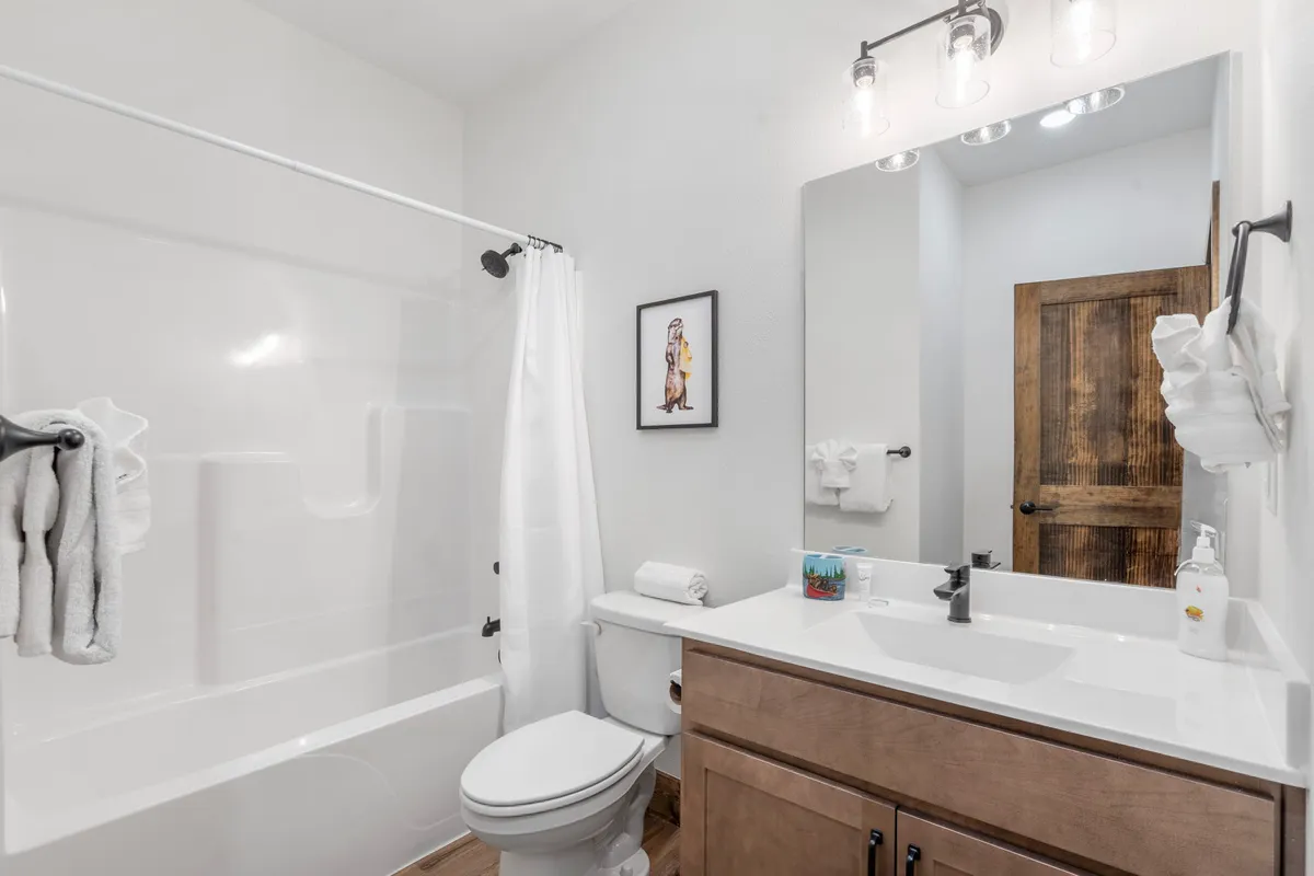 A sparkling ensuite bathroom with a vanity and sink, framed artwork, and a bathtub. The inviting space is well-lit and fresh, ideal for morning rituals or a relaxing soak.