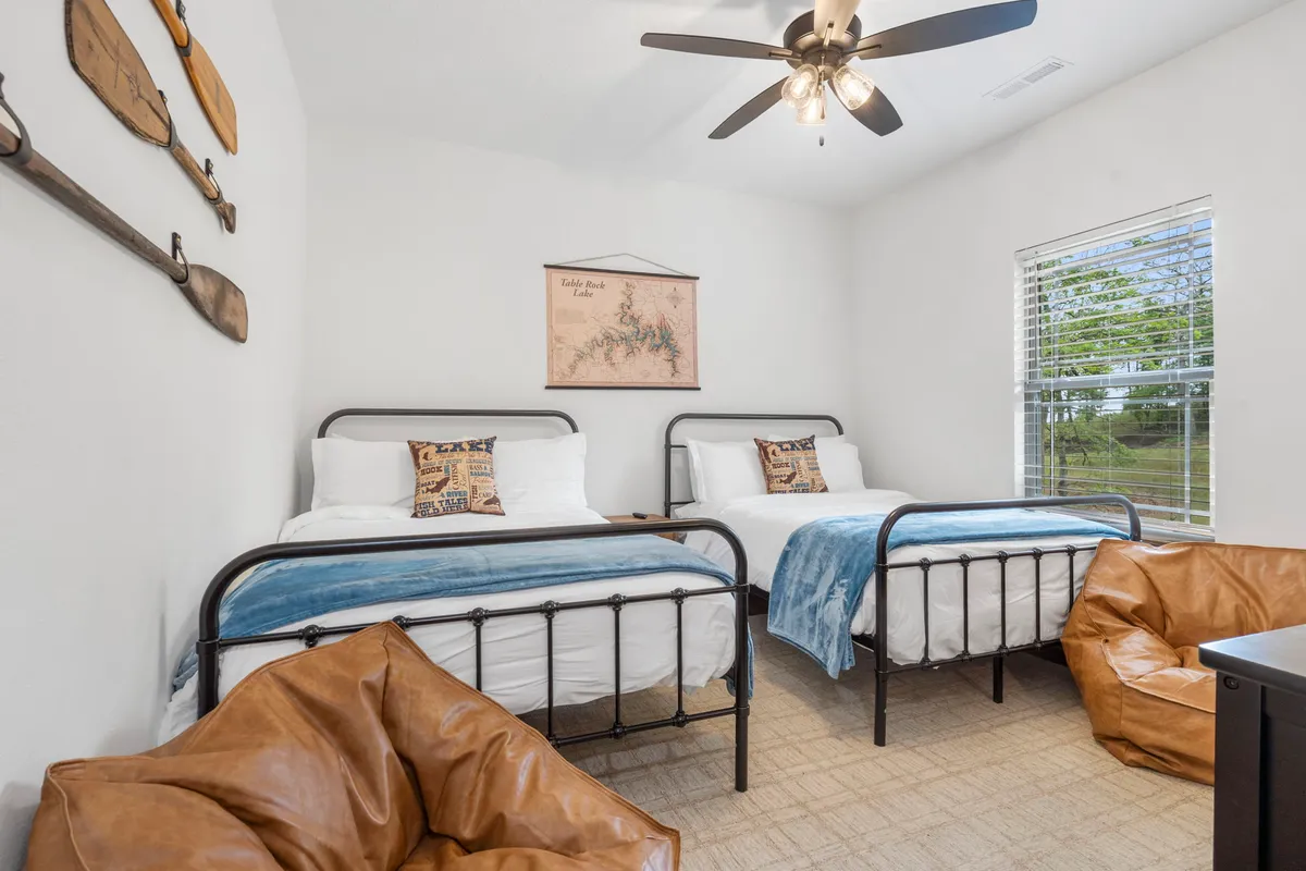 A welcoming twin bedroom with two metal bed frames, blue throw blanket, decorative pillows, map artwork, and bean bag chairs. The décor is playful yet modern, complementing the needs of families with children.
