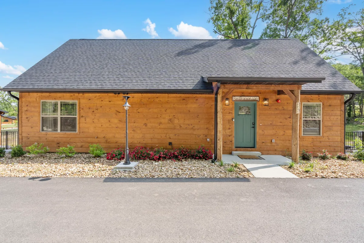 A cozy exterior view of a wooden facade with a green door, colorful flower beds, and a welcoming front porch, bathed in soft sunset light. The scene feels inviting, fresh, and ready for new guests to make it their own.